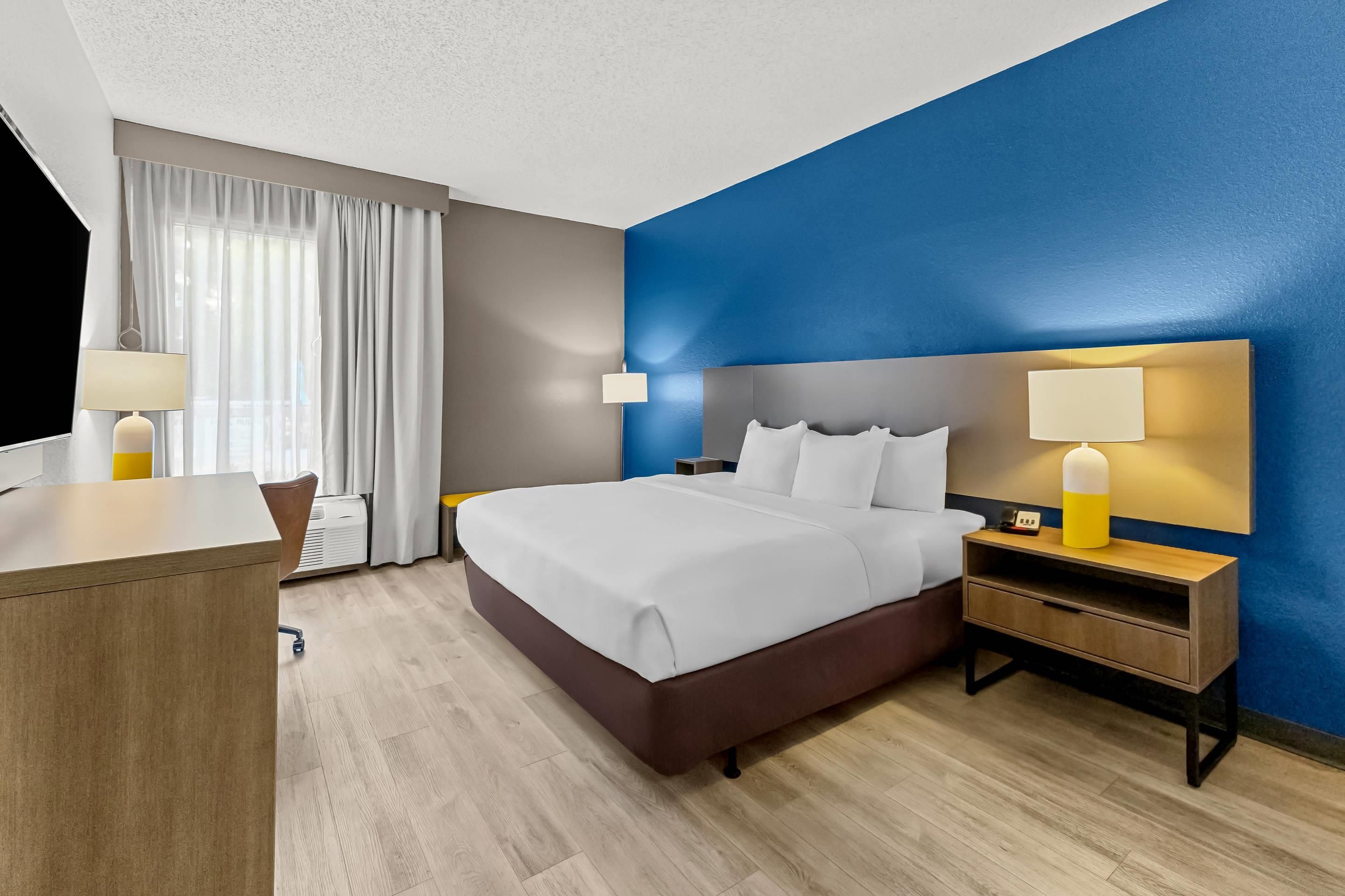 A hotel room with a bed, bedside tables, a desk, and a chair.