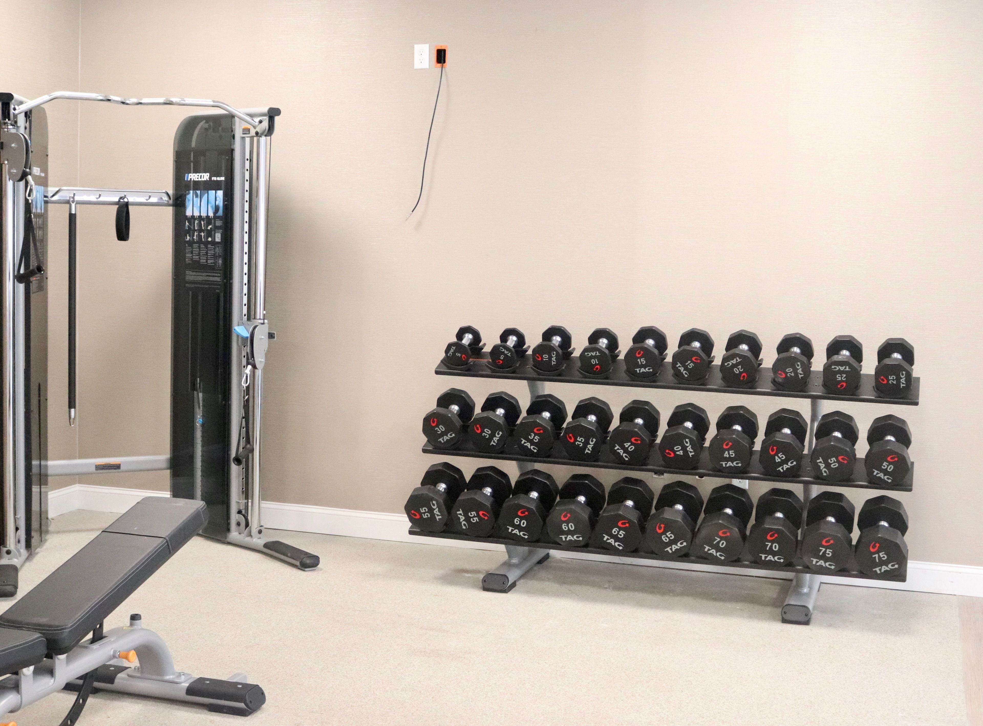 Ett gym med ett väggmonterat ställ för hantlar, en stång för chins och en träningsbänk.