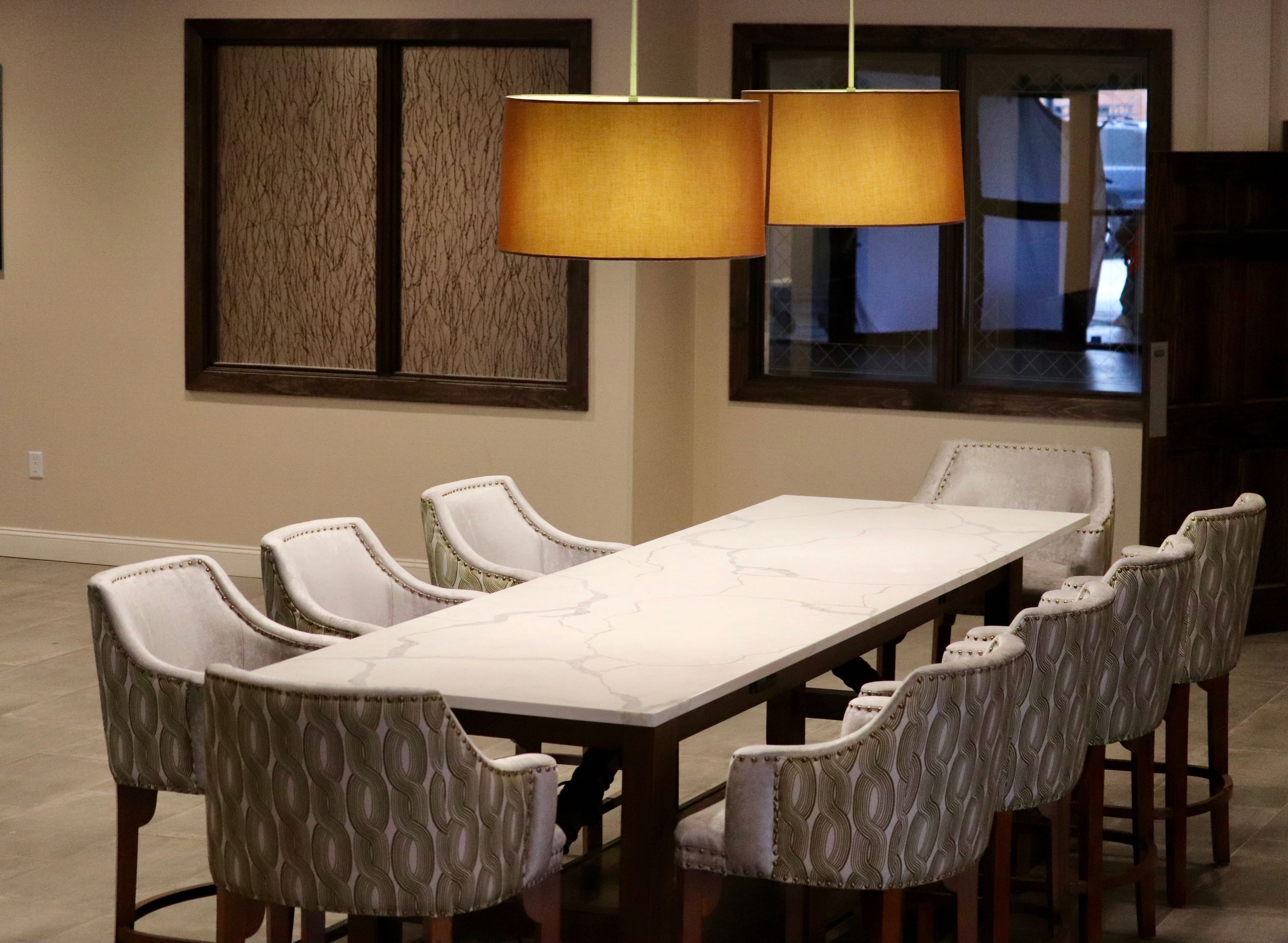 Uma área de refeições com uma mesa comprida e cadeiras estampadas, duas luminárias pendentes e um painel decorativo na parede.
