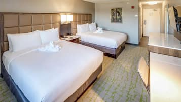 A hotel room with two beds, a desk, a mirror, and a bathroom door.