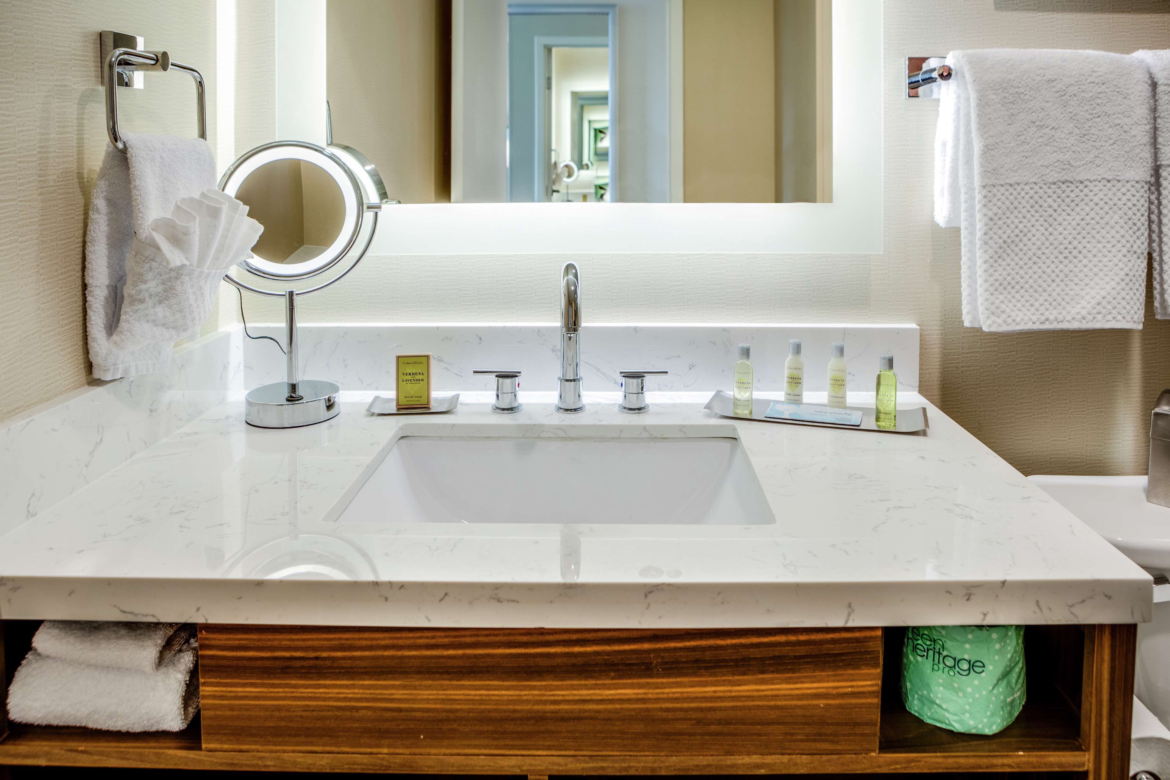A bathroom with a white marble sink, a round mirror, and a towel rack.