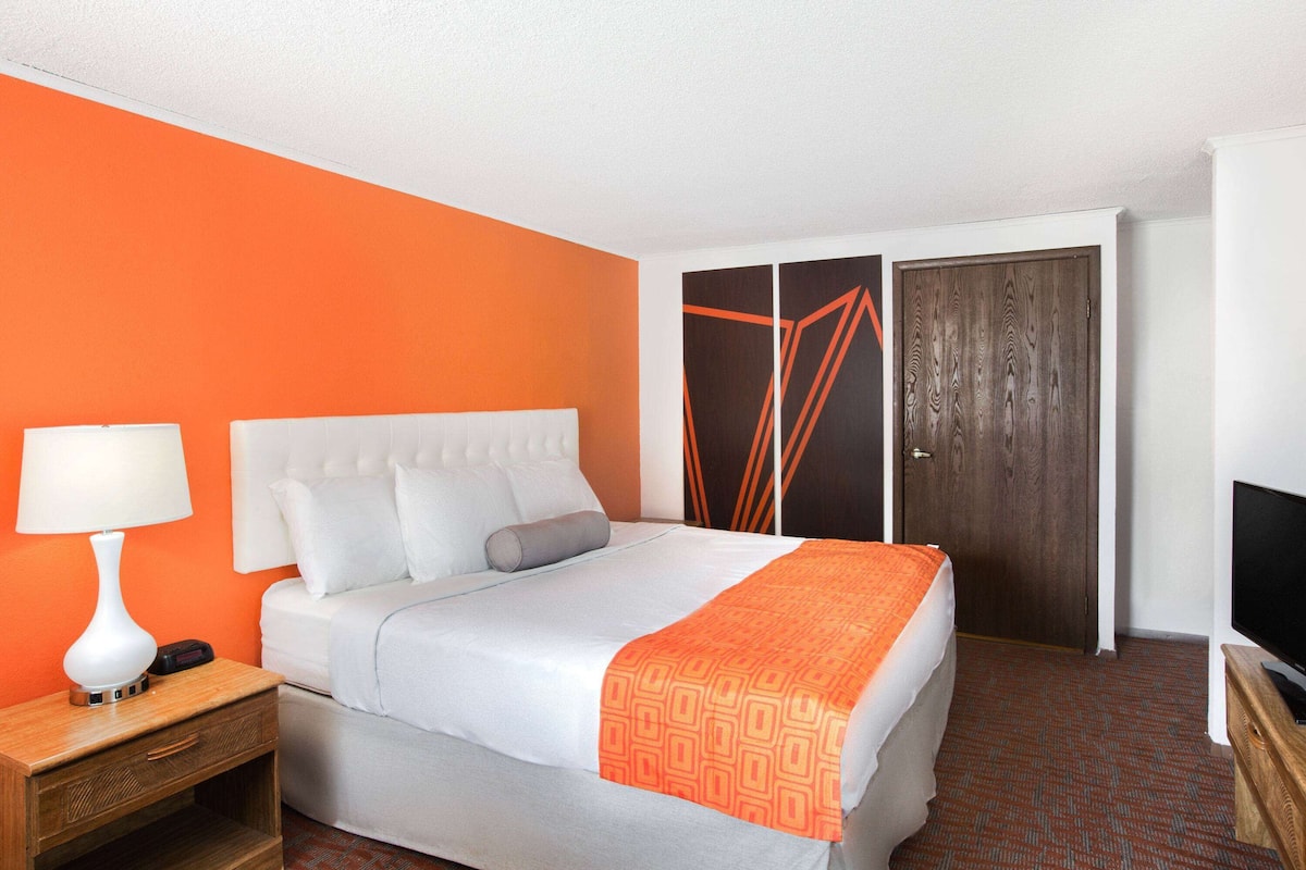 A hotel room with a bed, a nightstand, a lamp, a TV, and a wardrobe.