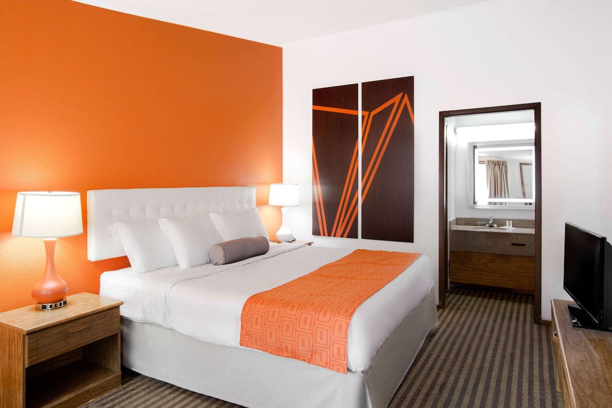 A hotel room with a bed, a nightstand, a TV, a mirror, and a bathroom with a sink and mirror.
