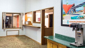 Habitación de hotel con alfombra estampada, una cafetera, un armario de madera y un cuadro en la pared.