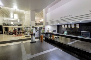Um hall de hotel moderno, com balcão de recepção, área de estar e escada para um andar superior.