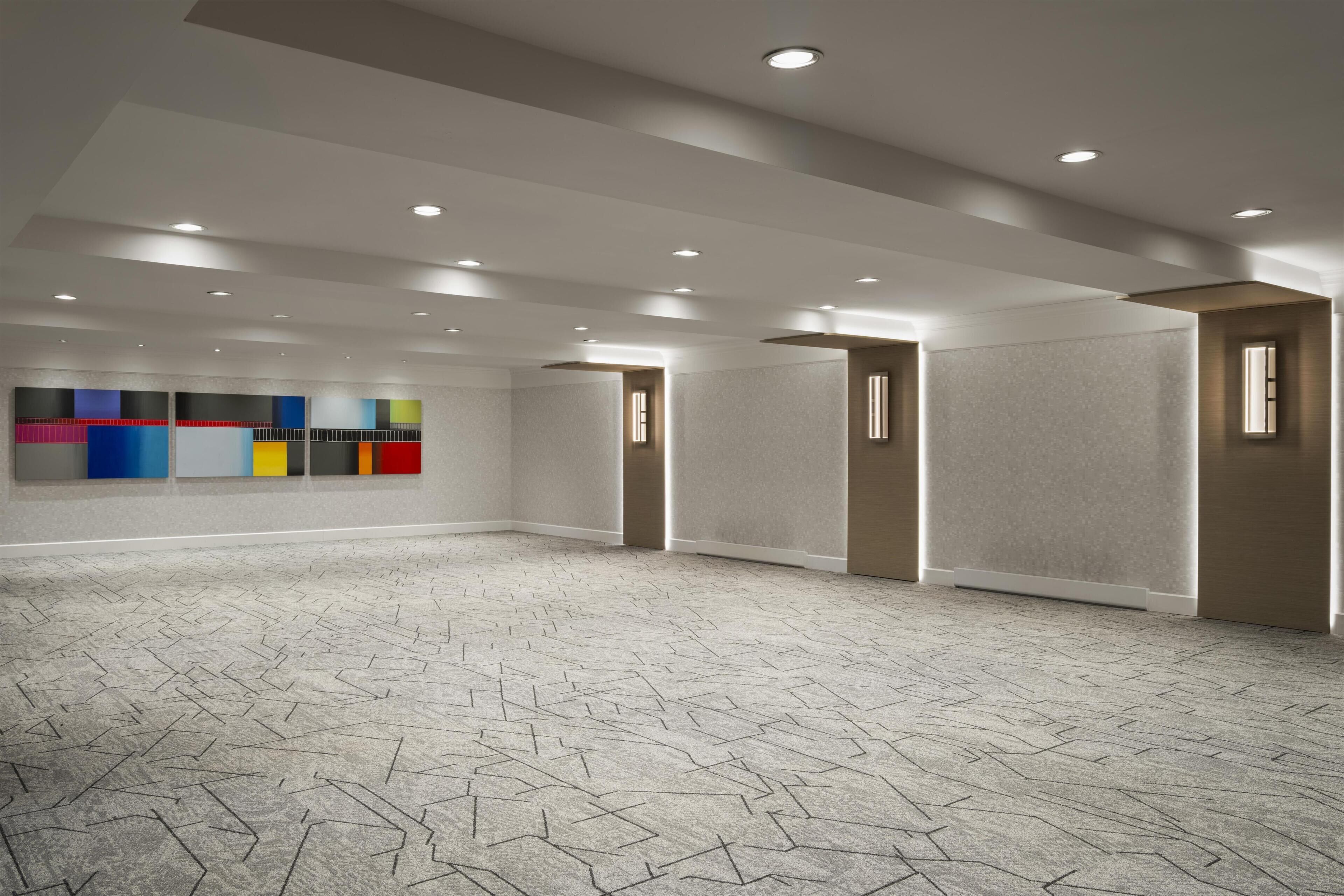 A spacious room with a patterned carpet, recessed ceiling lights, a wall with colorful panels, and a door with a window.