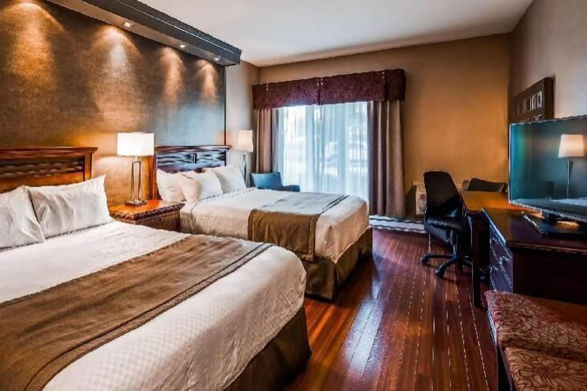 A hotel room with two beds, a desk, a TV, and a window with curtains.
