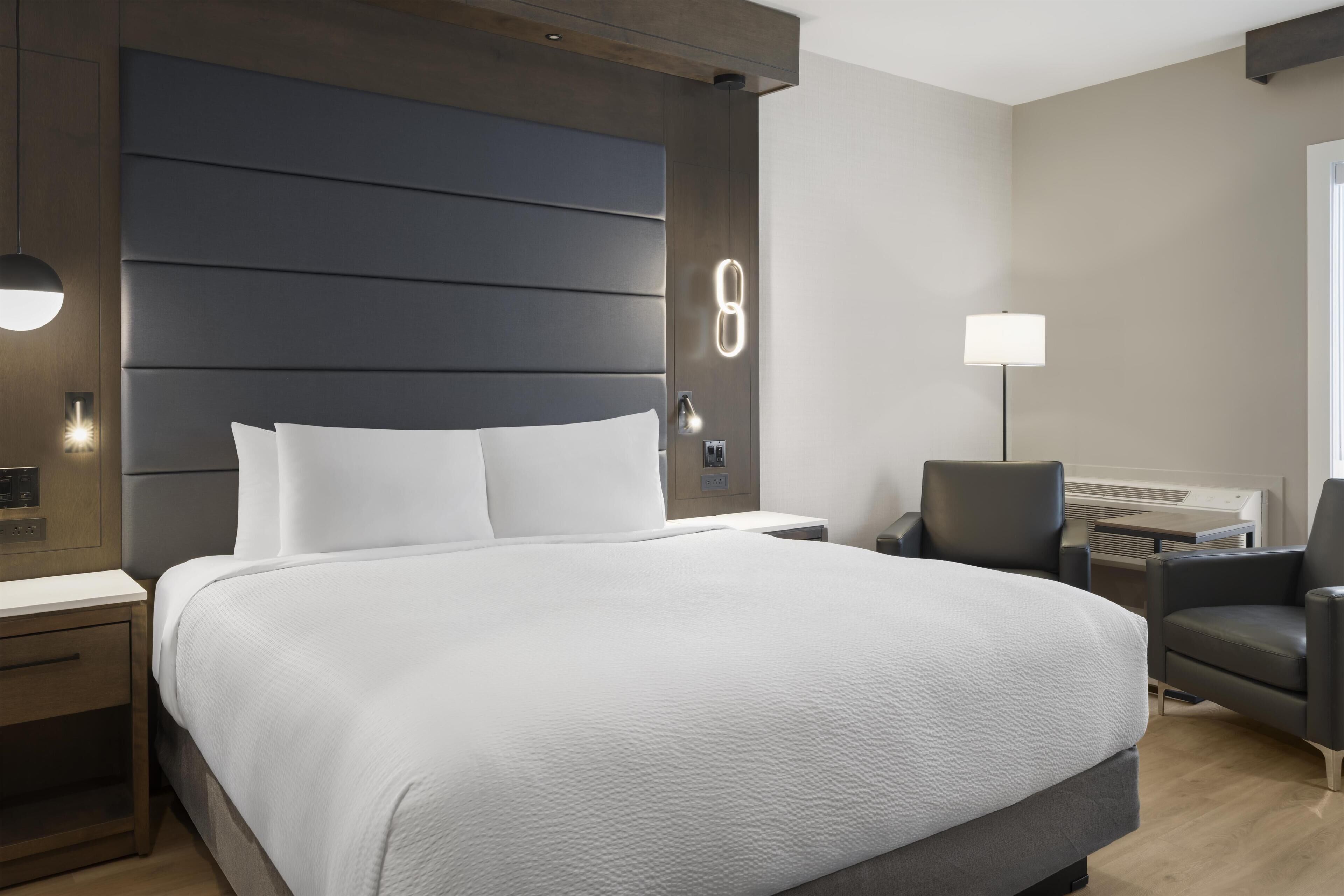 Une chambre d’hôtel moderne équipée d’un grand lit, d’un bureau, d’une chaise et d’une lampe fixée au mur.