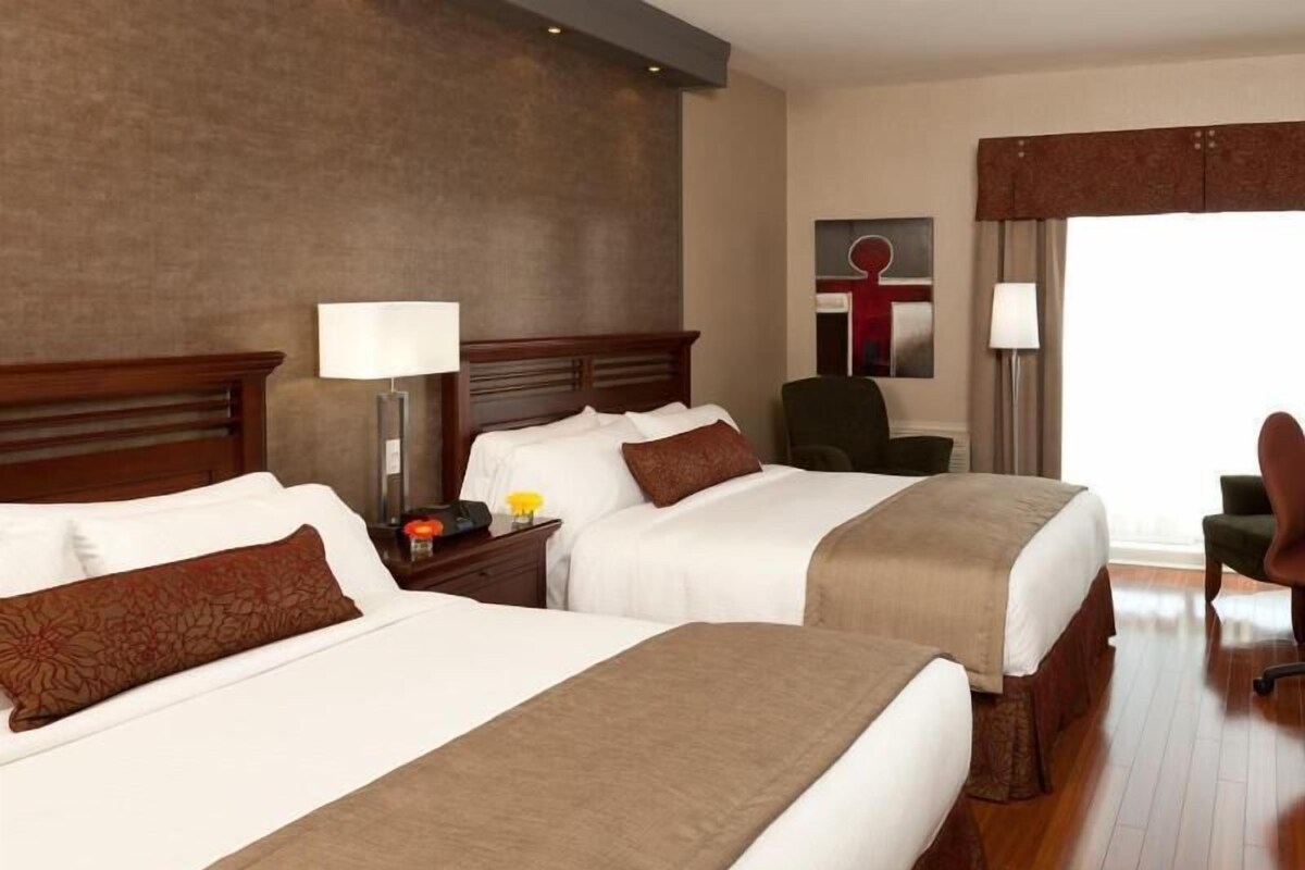 Habitación de hotel con dos camas, un escritorio, una silla y un ventanal.