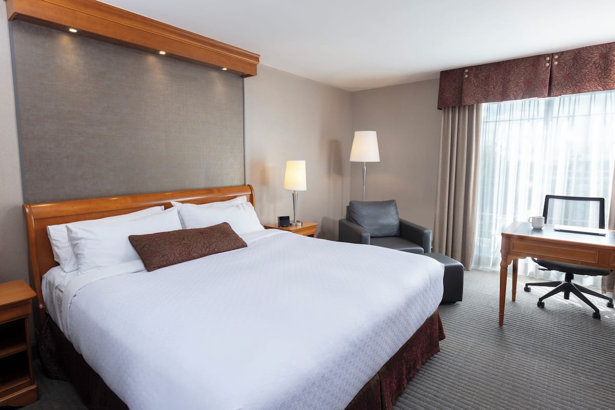 A hotel room with a large bed, a desk, a chair, and a lamp.