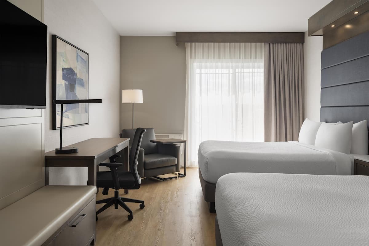 A hotel room with a bed, a desk, a chair, a TV, and a window with curtains.