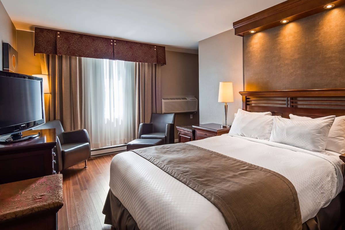 A hotel room with a bed, bedside lamps, a desk with a television, a chair, and a large window with curtains.