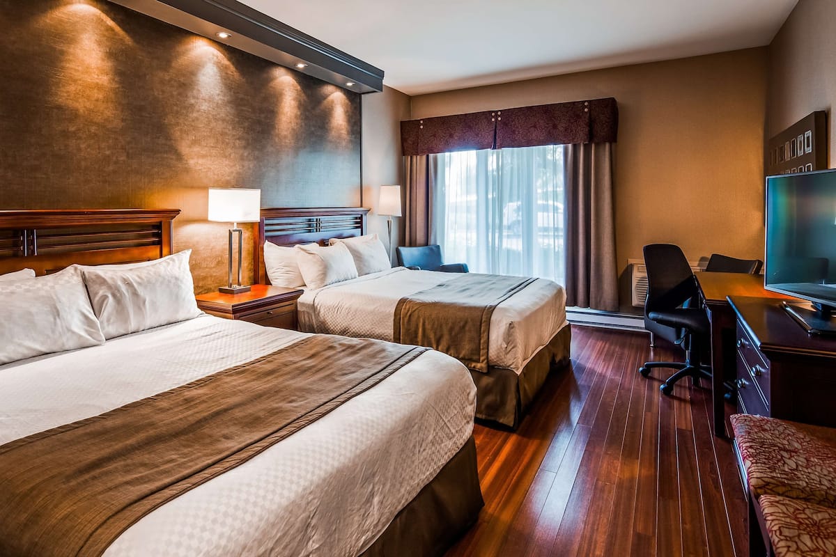 A hotel room with two beds, a desk with a television, and a chair.