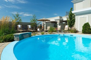 A swimming pool with lounge chairs and umbrellas, surrounded by greenery and a building. - Best Western Premier Hotel Aristocrate (Québec City)