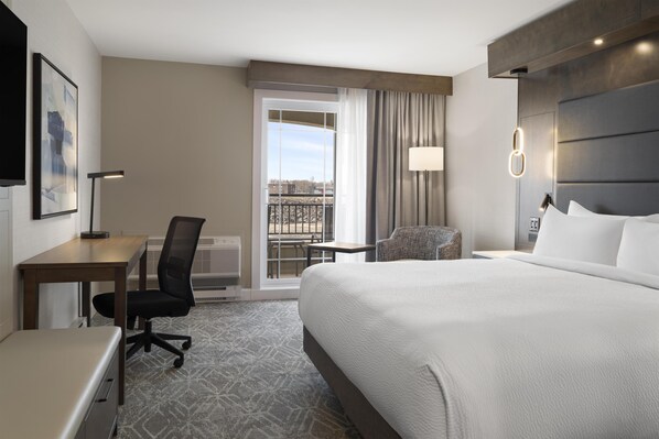 A hotel room with a large bed, a desk, a chair, a lamp, and a view of the city through a balcony. - Best Western Premier Hotel Aristocrate (Québec City)