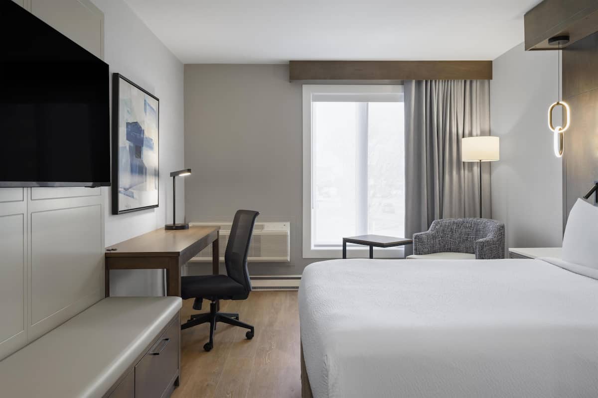 A hotel room with a bed, desk, chair, TV, and a window with curtains.