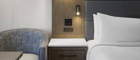 A hotel room with a bed, bedside table, lamp, and a wall-mounted light fixture.