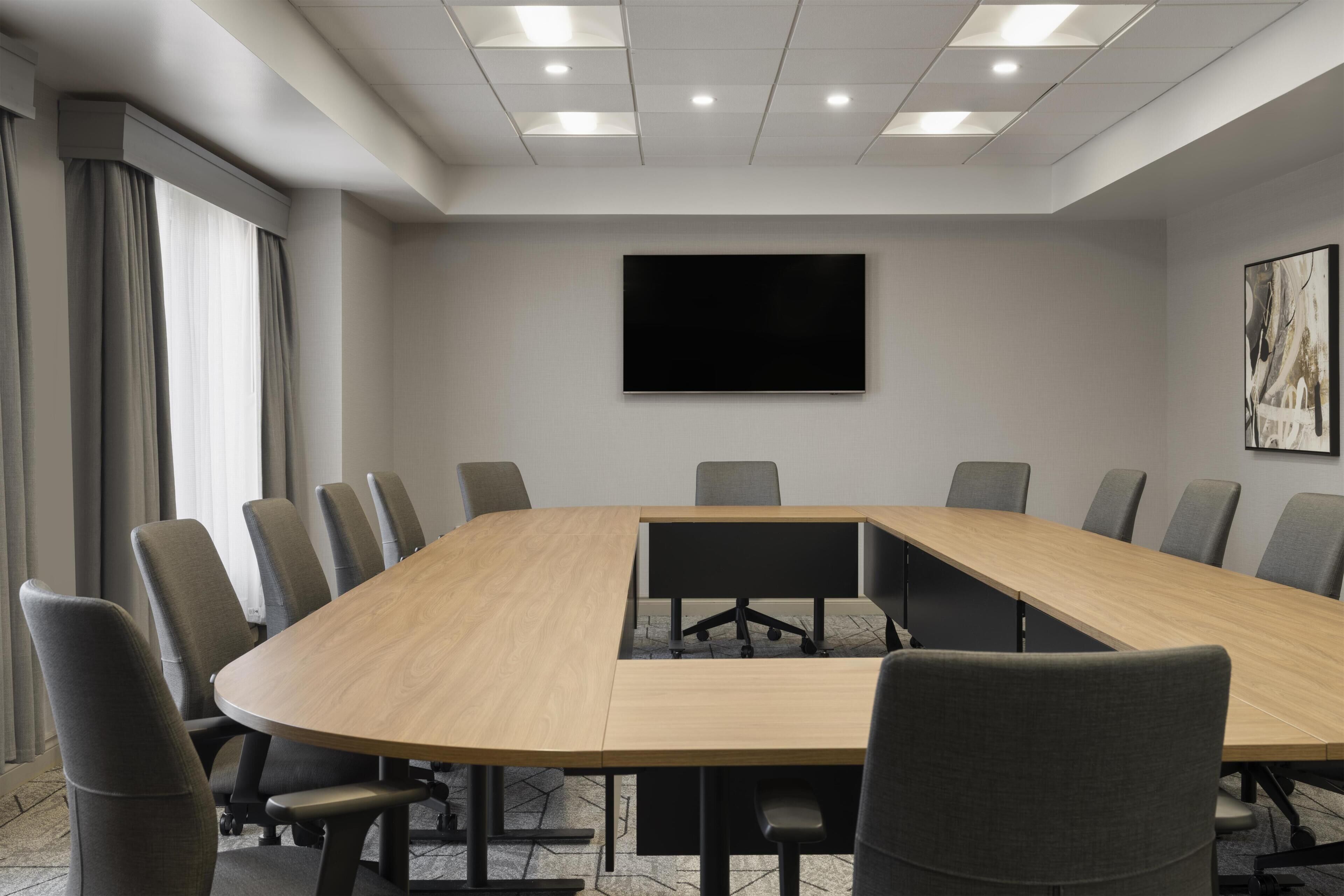 A conference room with a long table, chairs, a flat-screen TV, and a painting on the wall.