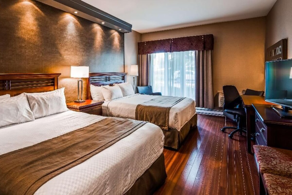 Habitación de hotel con dos camas, un escritorio, una silla, un televisor y una ventana con cortinas.