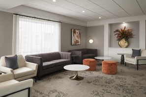 A modern living room with a grey sofa, a white armchair, a round coffee table, and a small orange ottoman. - Best Western Premier Hotel Aristocrate (Québec City)
