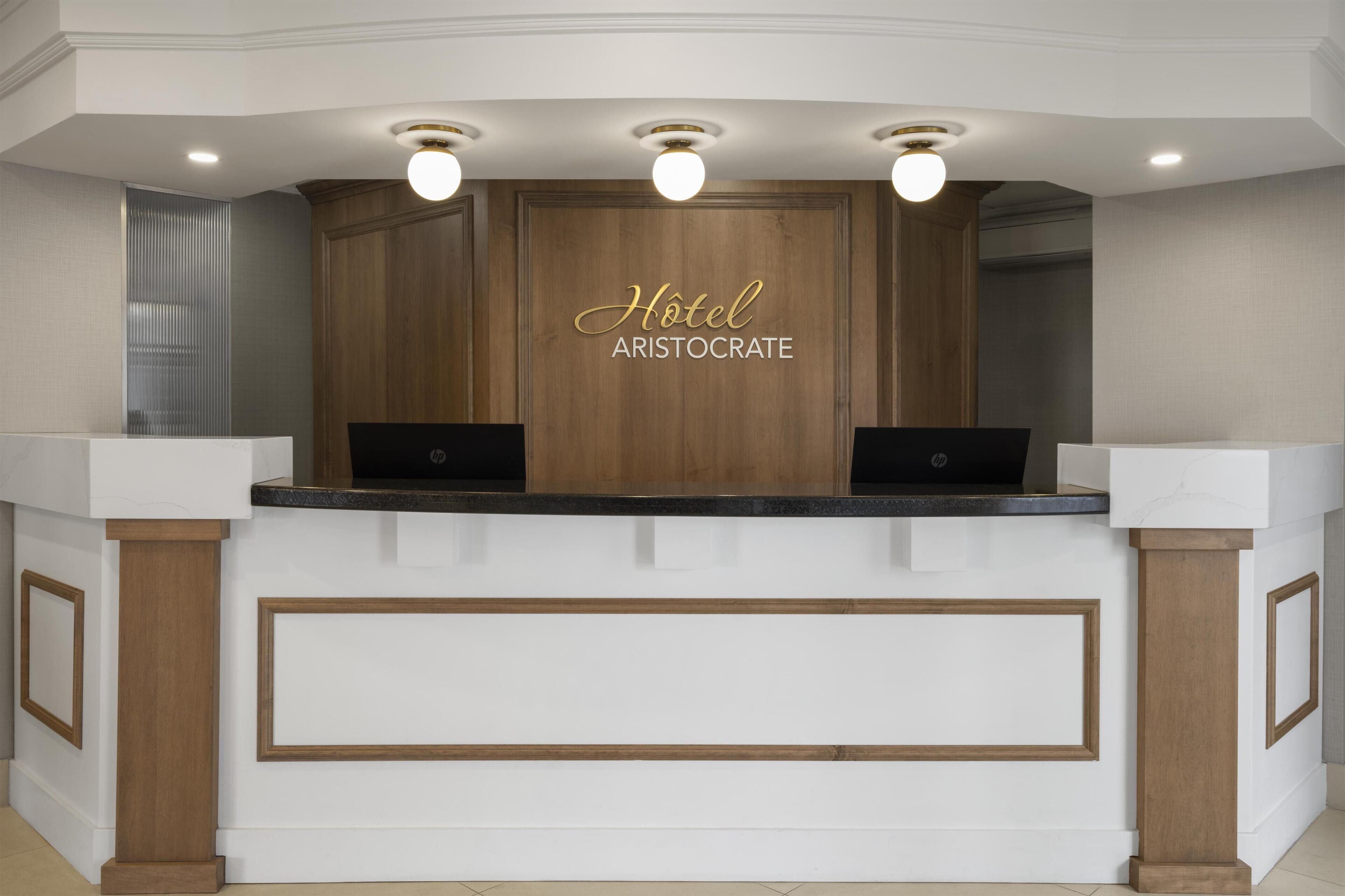 Un mostrador de recepción con fondo de madera, dos computadoras portátiles y un cartel que dice 'Hotel Aristocrate'.