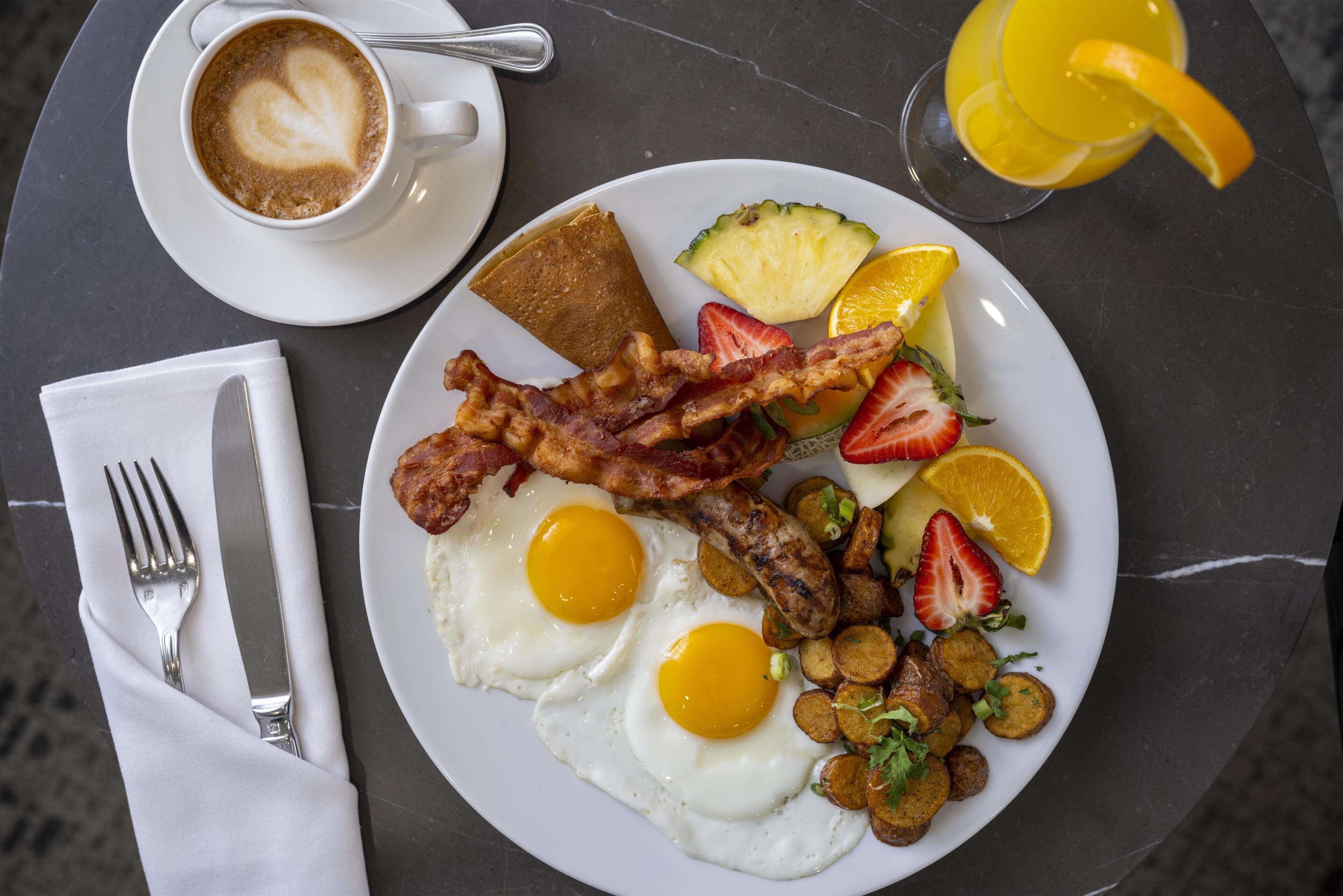 A breakfast plate with eggs, bacon, toast, fruit, and potatoes.