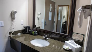 A hotel bathroom with a granite countertop, a white sink, a hairdryer, a mirror, and a towel rack.