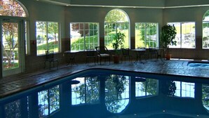 An indoor swimming pool with clear views of the outdoors through large windows. - Hotel Grand Victorian (Branson)