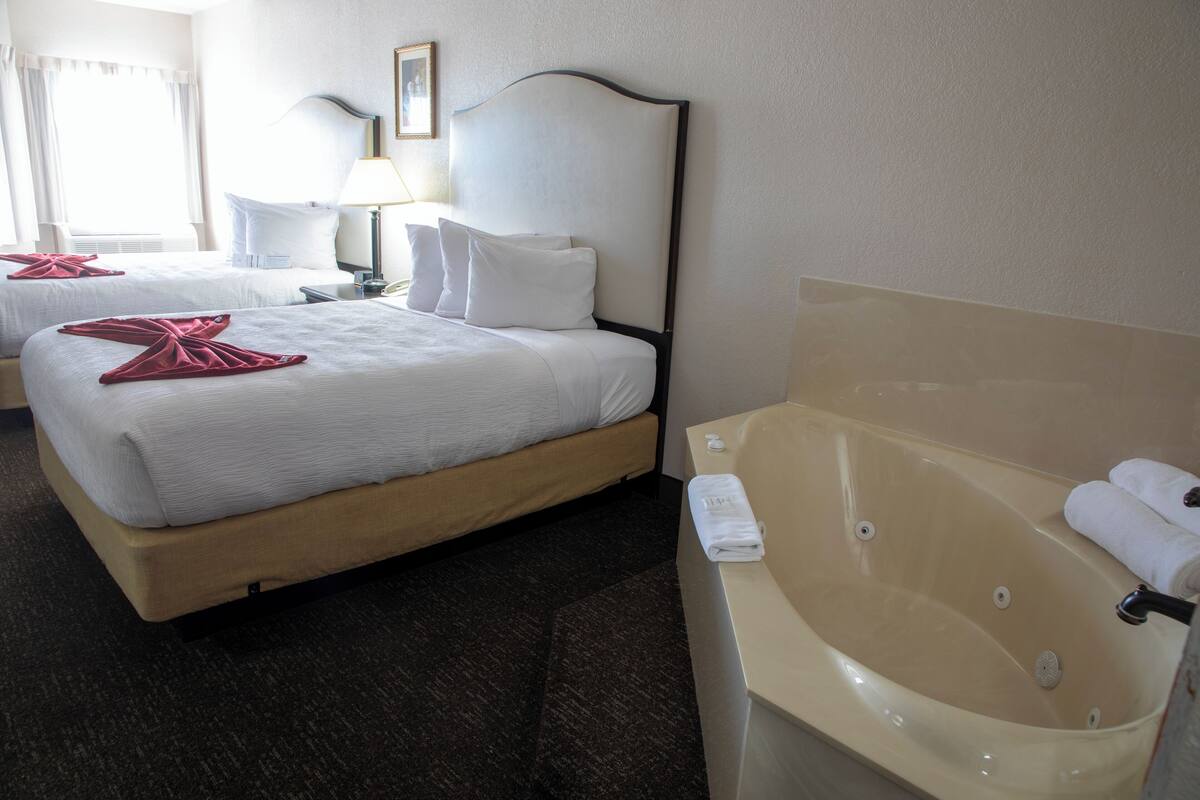 A hotel room with two beds, a large bathtub, and a nightstand with a lamp.