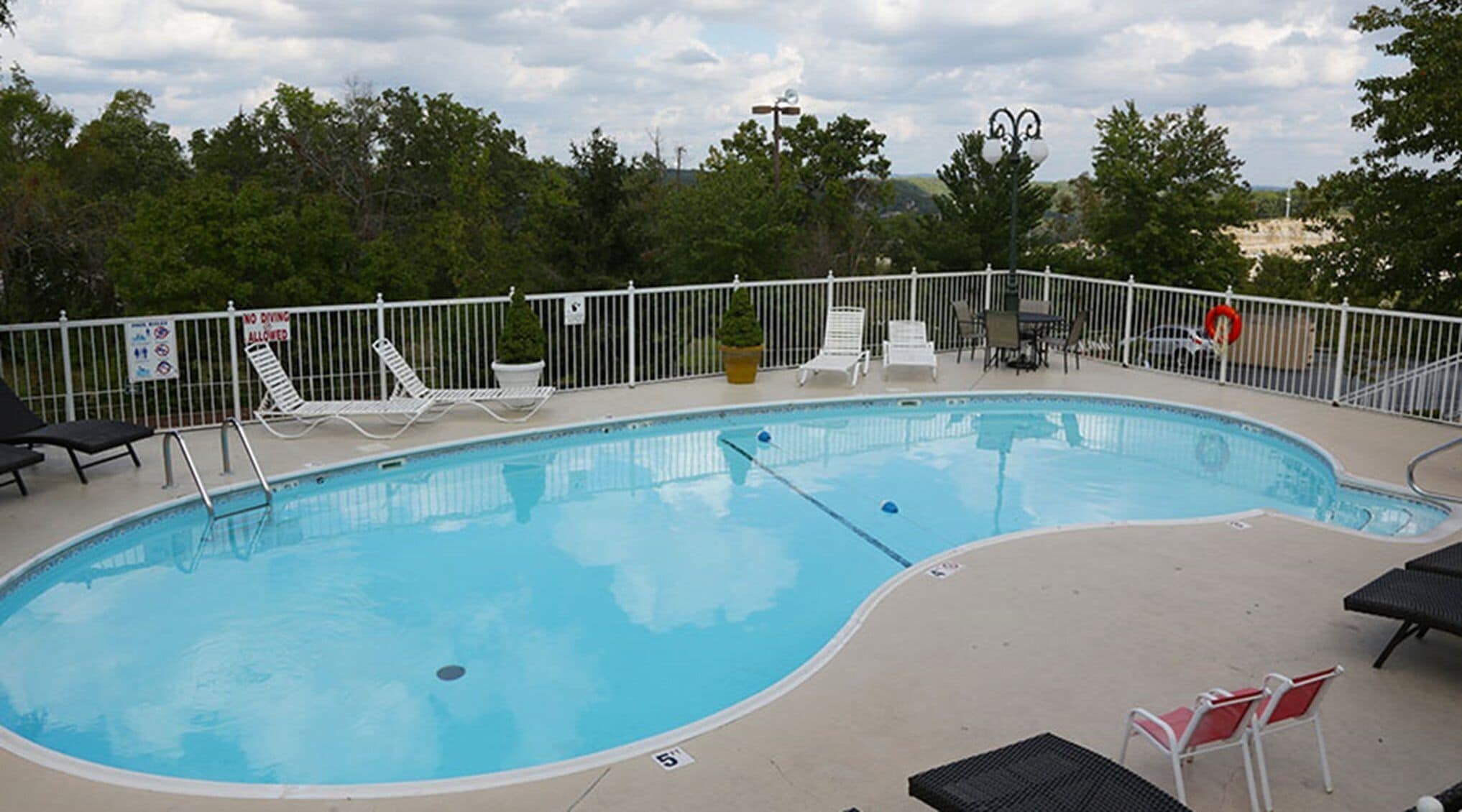 A swimming pool with a white fence, lounge chairs, and a lifebuoy.