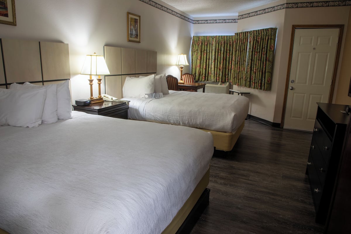 A hotel room with two beds, a desk, a chair, a lamp, a telephone, and a door.