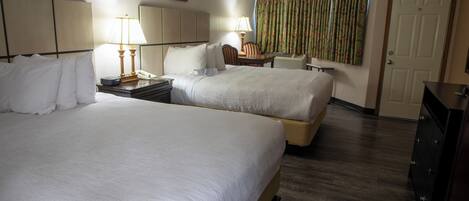 A hotel room with two beds, a desk, a chair, a lamp, a telephone, and a door.