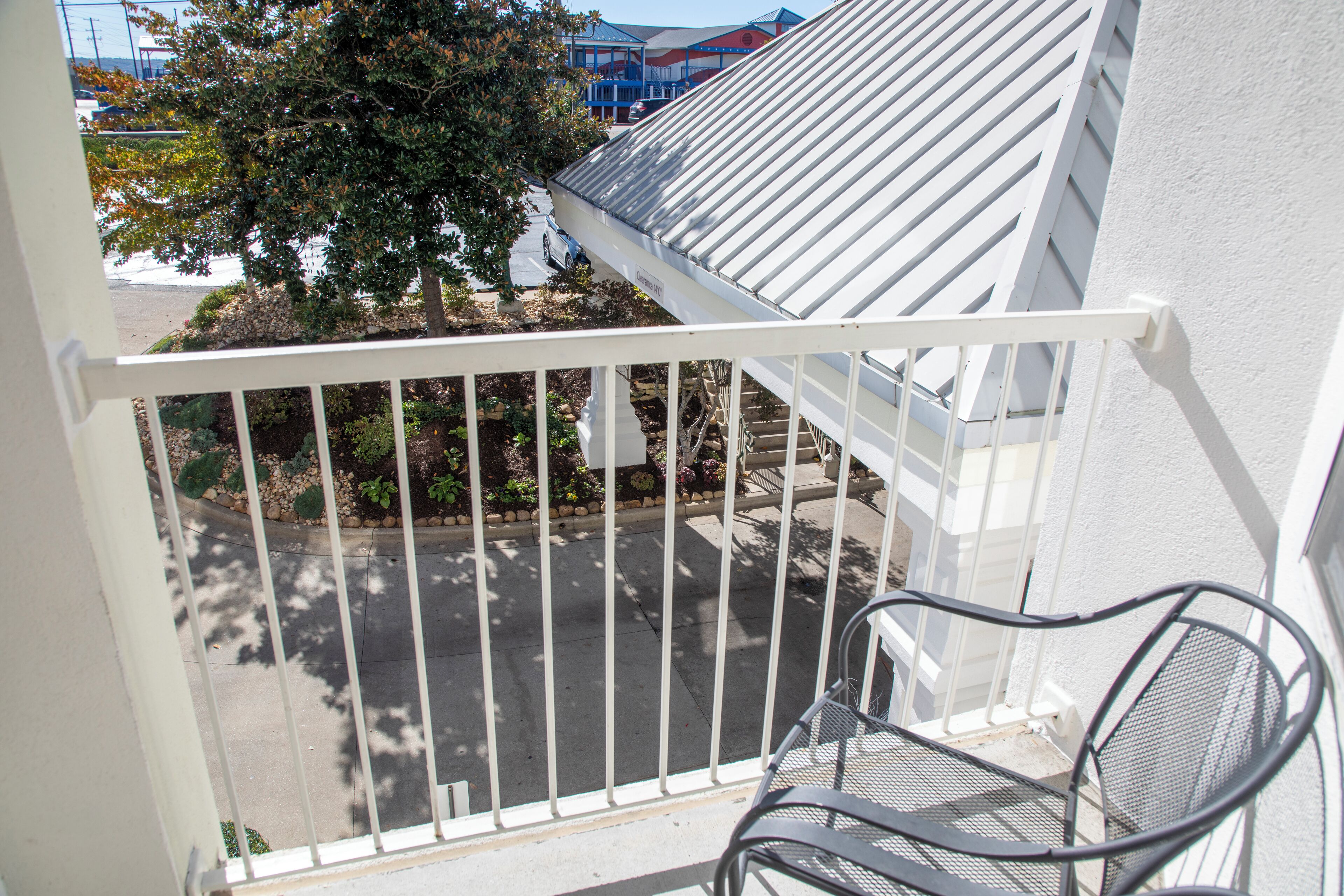 A balcony with a metal chair, white railing, and a view of a parking lot and buildings.
