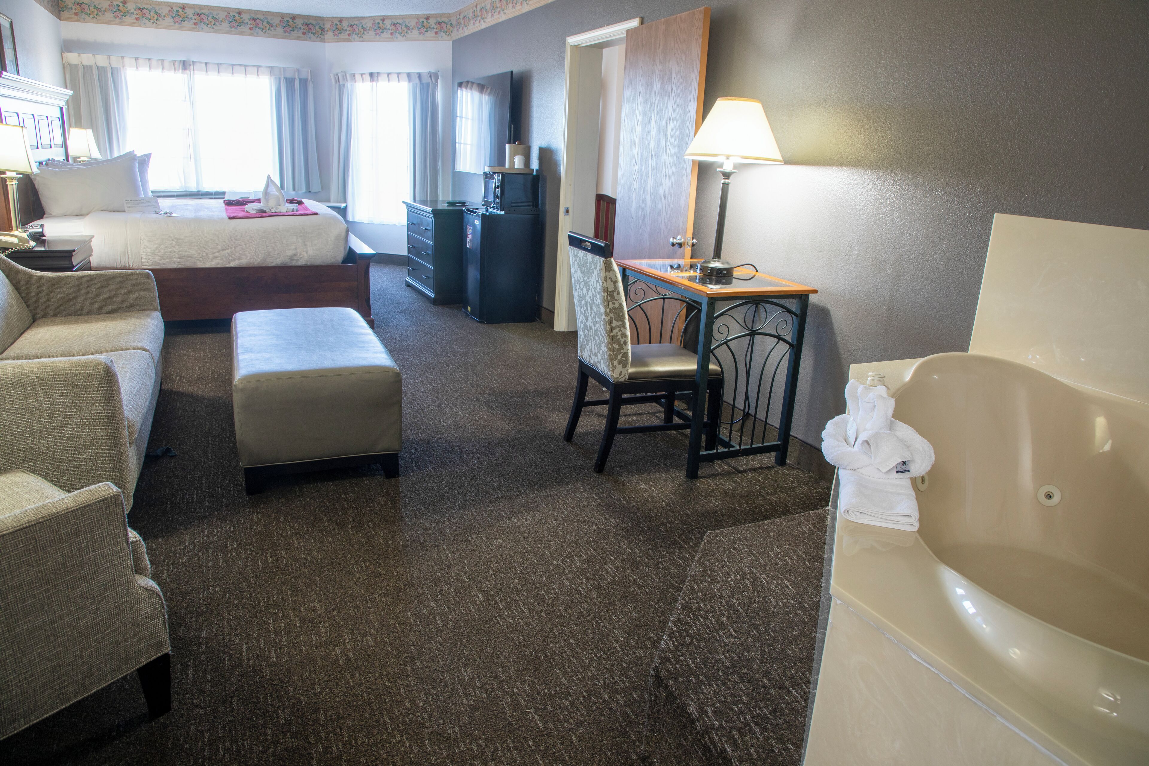 Une chambre d’hôtel comprenant un lit, un bureau, une chaise, un canapé, une petite table, une baignoire et un téléviseur.