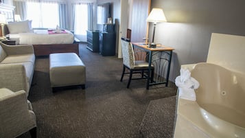 A hotel room with a bed, a desk, a chair, a sofa, a small table, a bathtub, and a television.
