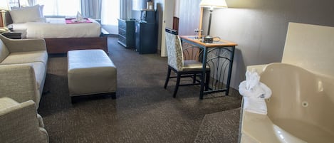 A hotel room with a bed, a desk, a chair, a sofa, a small table, a bathtub, and a television.