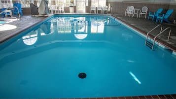 An indoor swimming pool with clear blue water, surrounded by blue and white chairs, and a sign indicating no lifeguard on duty.