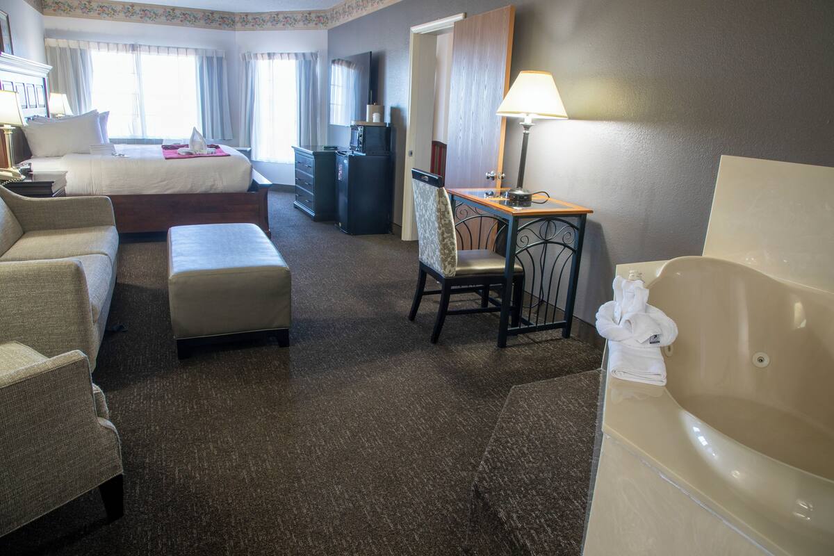 A hotel room with a bed, a desk, a chair, a sofa, a small table, and a bathtub.