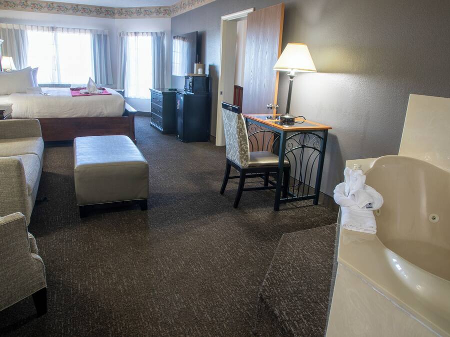 Habitación de hotel con cama, escritorio, silla, sofá, mesita pequeña y bañera.