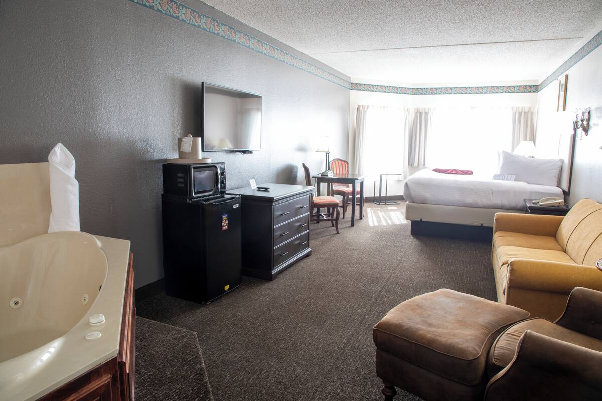 A hotel room with a bed, a sofa, a desk with a computer, a television, and a bathroom with a bathtub.