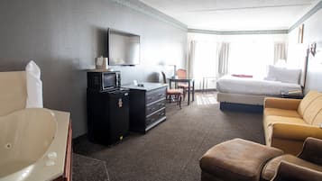 A hotel room with a bed, a sofa, a desk with a computer, a television, and a bathroom with a bathtub.