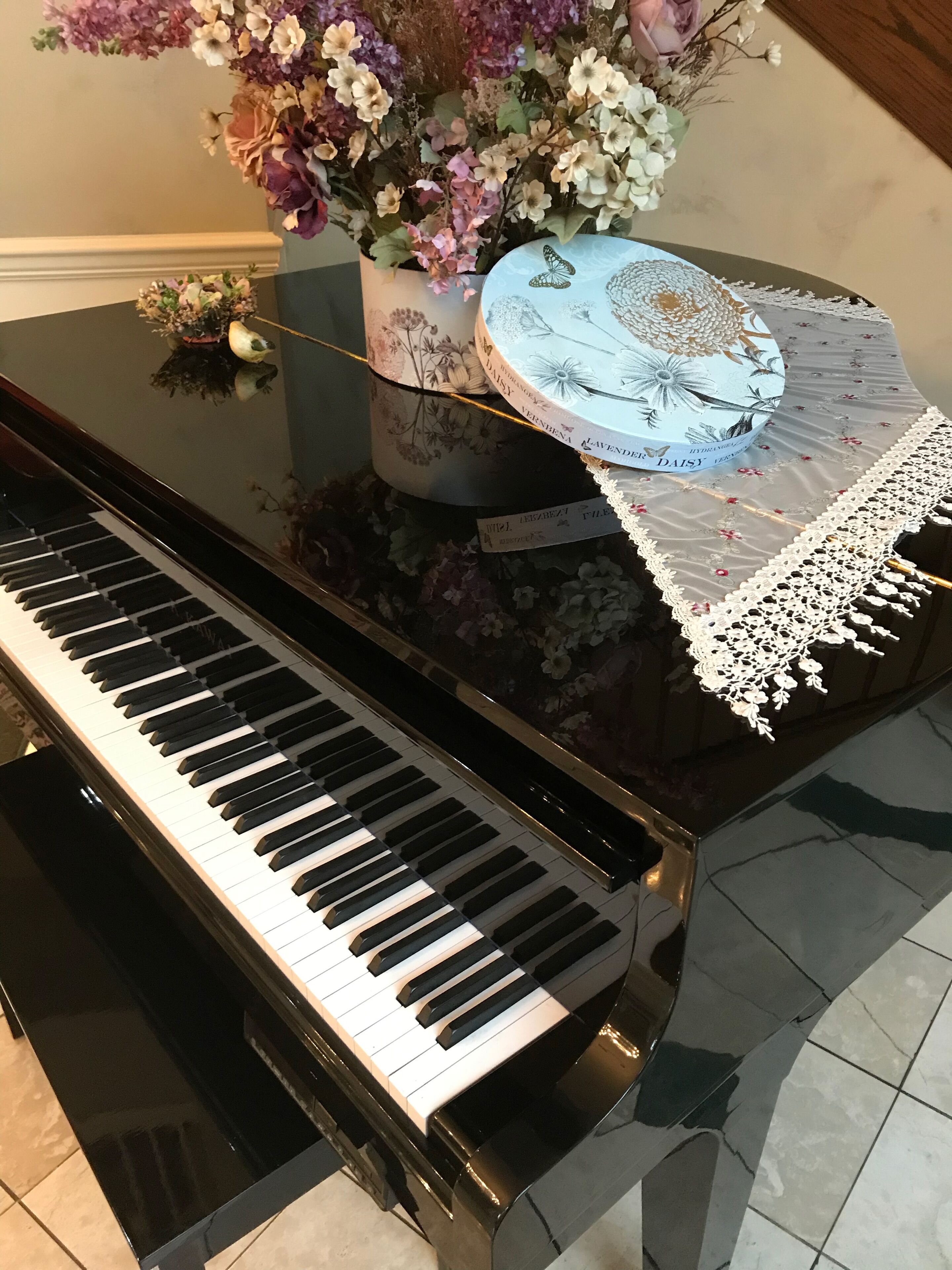 A grand piano with a floral arrangement and a decorative box on its stand.