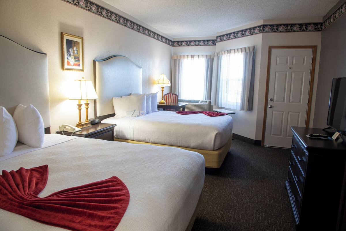A hotel room with two beds, a desk with a lamp, a chair, a dresser, and a television.