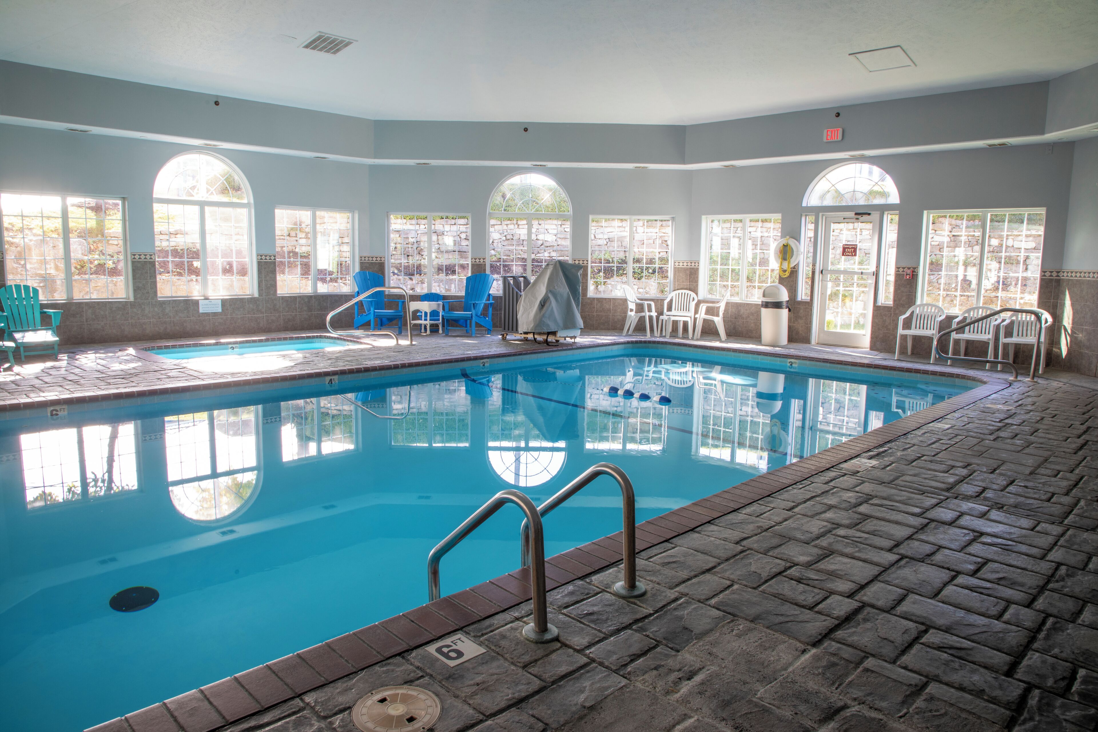 A swimming pool with a tiled deck, surrounded by chairs and a covered seating area.