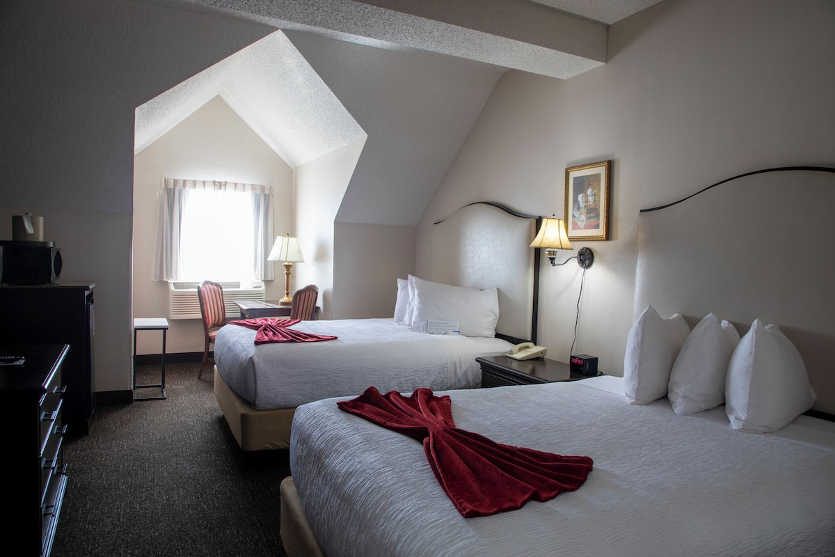 A hotel room with two beds, a desk, a chair, and a desk lamp.
