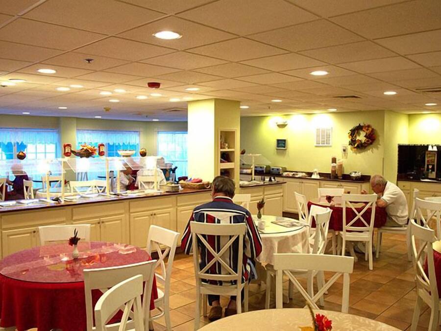A restaurant with multiple tables and chairs, a kitchen area, and a counter where food is being prepared.