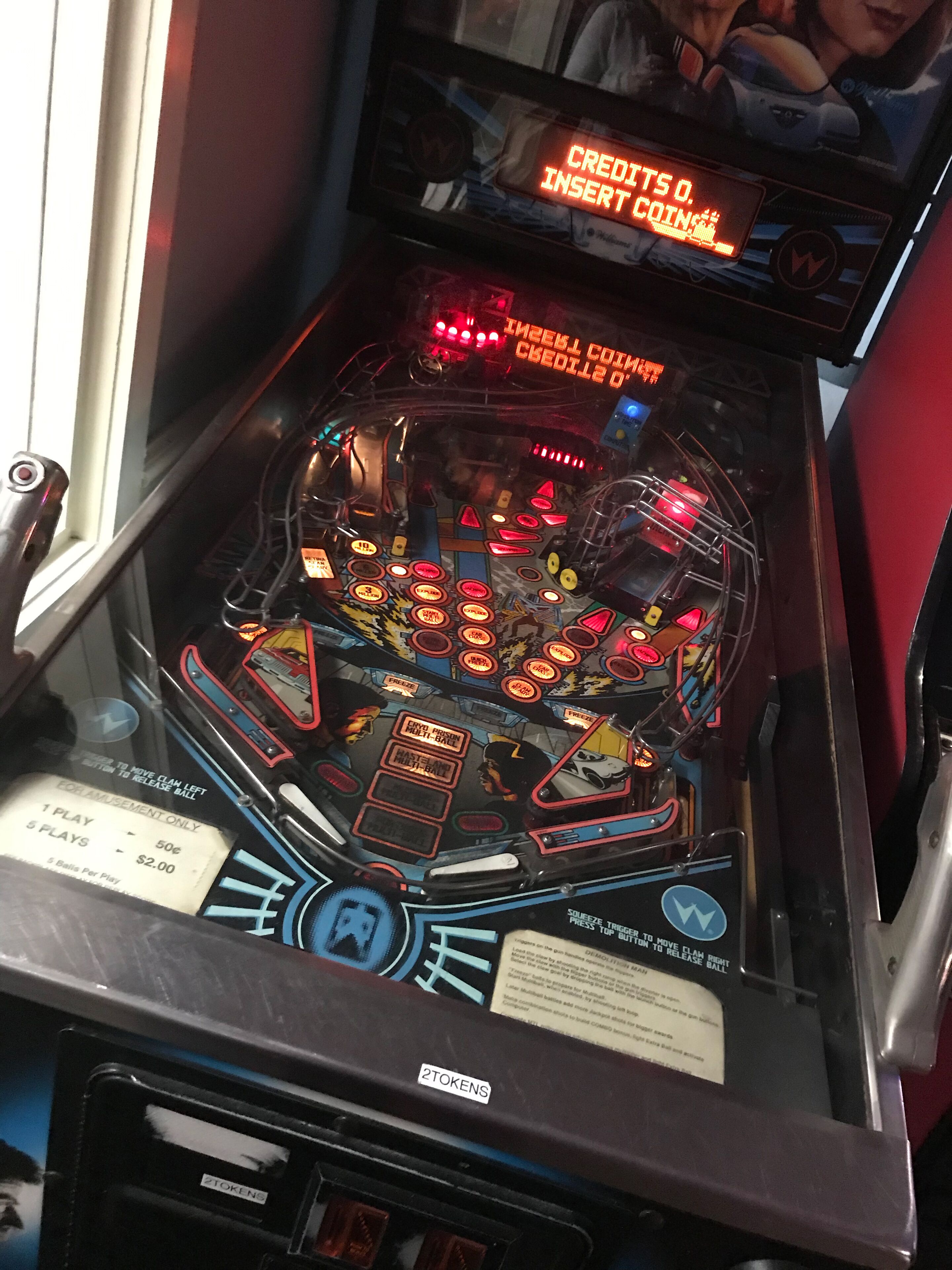 A pinball machine with a neon sign that reads "CREDITS O. INSERT COIN" and a label indicating "2 TOKENS".