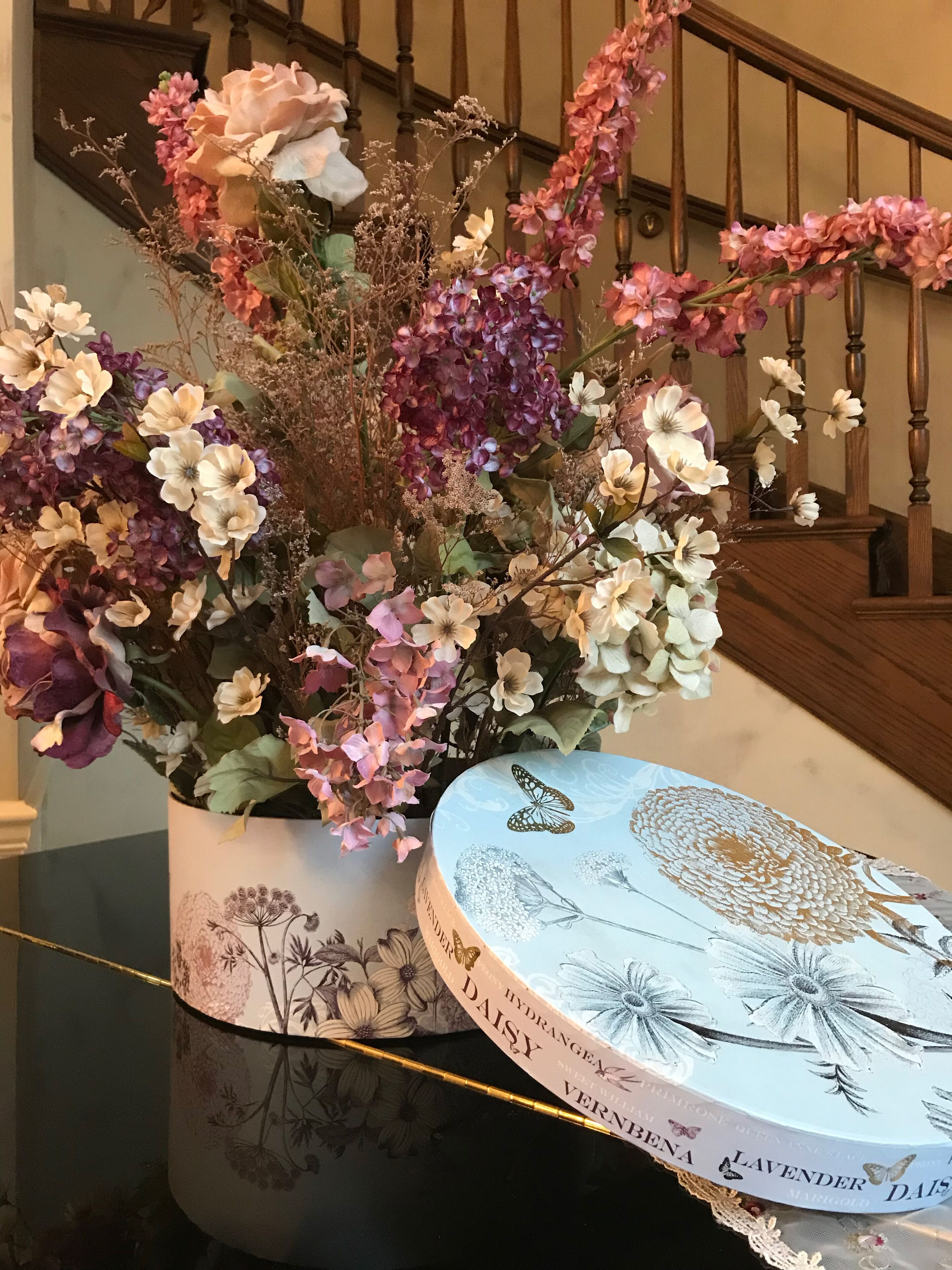 Een bloemstuk in een decoratieve vaas met een bloemenmotief, geplaatst op een tafel.