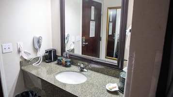 Une salle de bain dotée d’un comptoir en granit, d’un lavabo blanc, d’un sèche-cheveux, d’une machine à café et d’une poubelle.