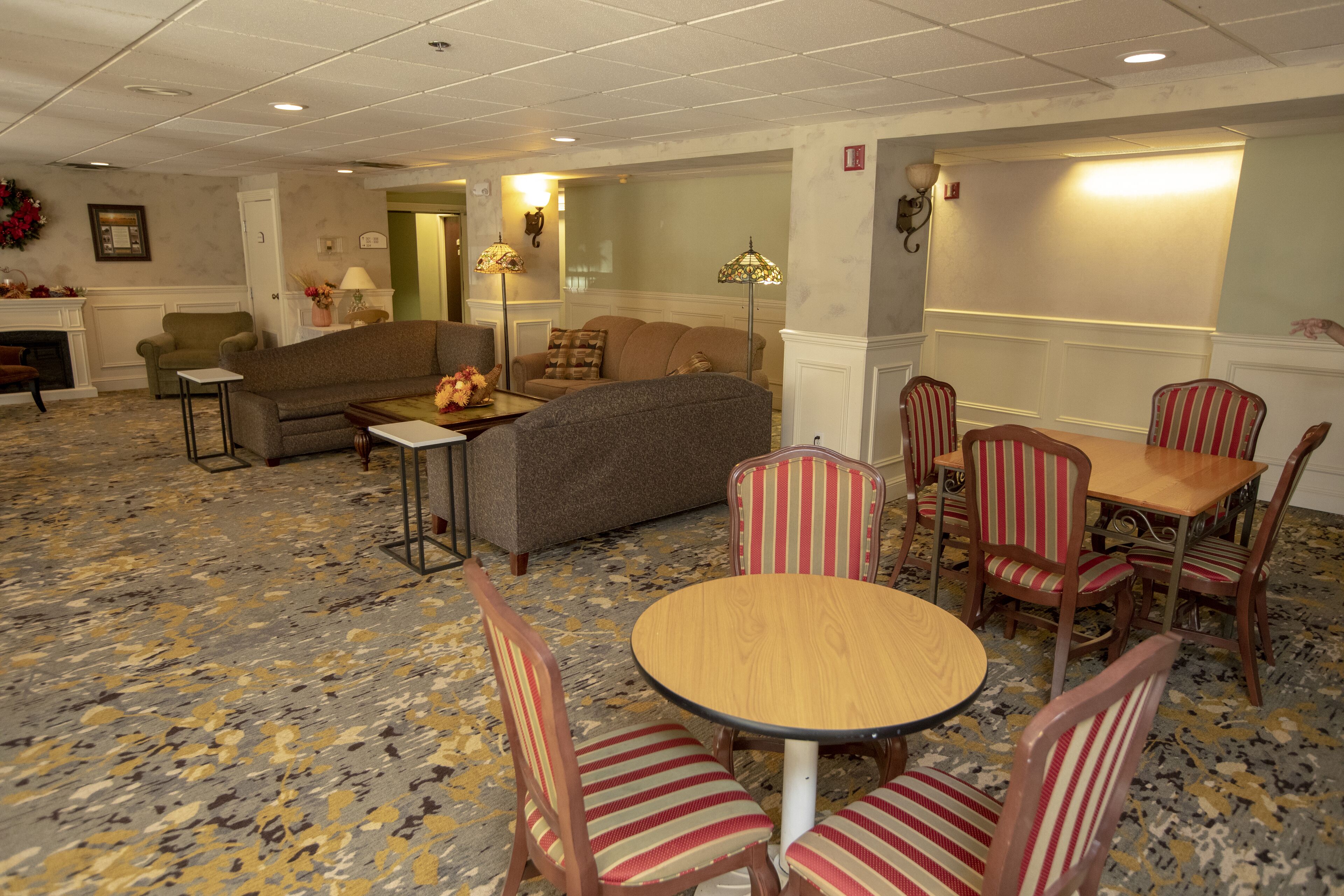 Un hall d’hôtel avec une table ronde en bois, des chaises à rayures, des canapés et une moquette à motifs.